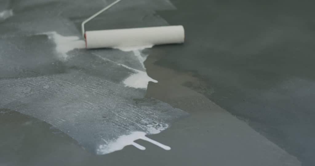 Applying white paint on a dark surface with roller.