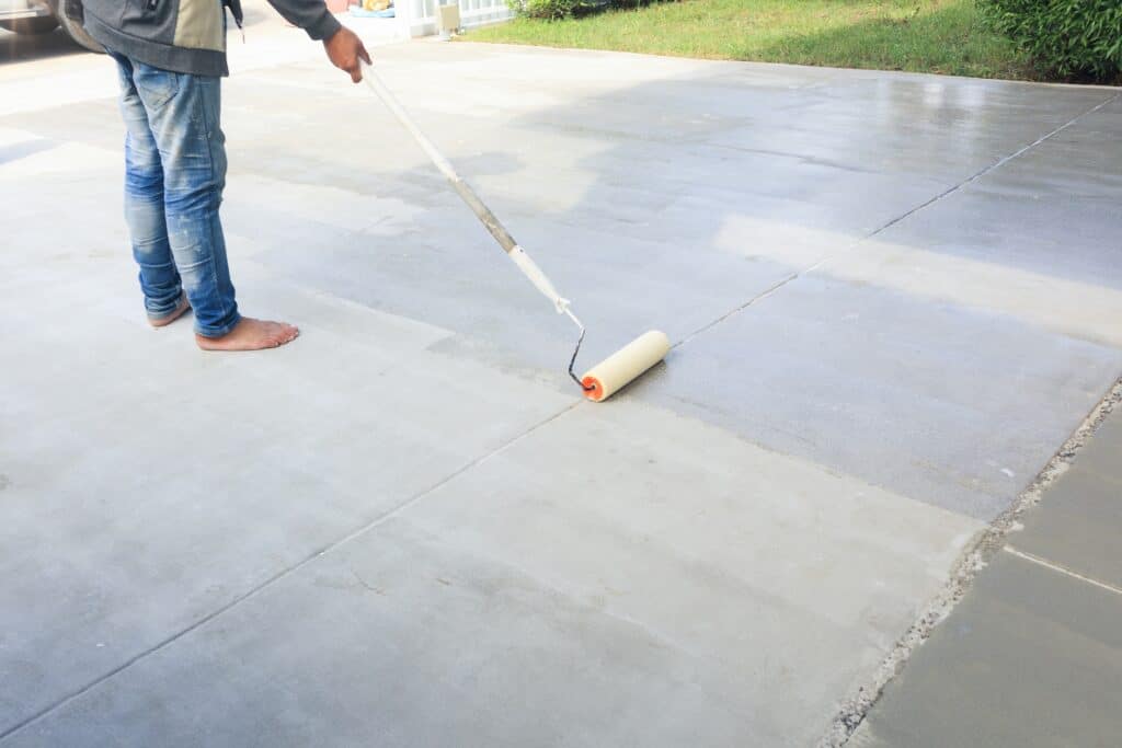 Person applying sealant on concrete driveway with roller