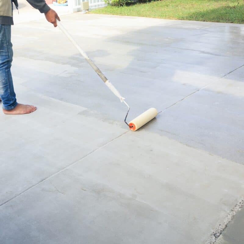 Person applying sealant on concrete driveway with roller