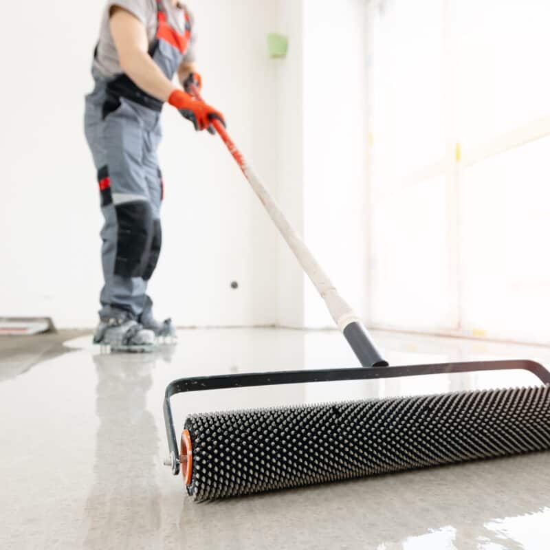Worker applying epoxy floor coating with roller.