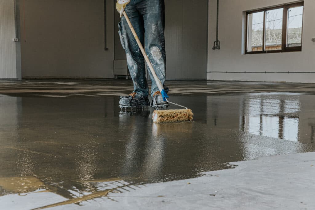 Worker spreading epoxy on concrete floor surface.