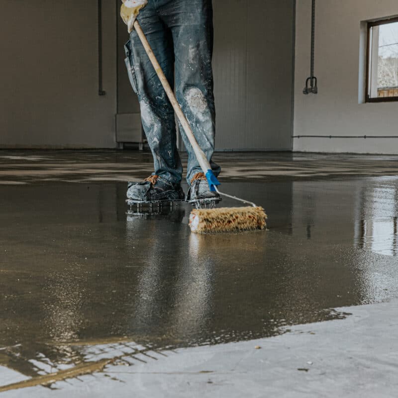 Worker spreading epoxy on concrete floor surface.