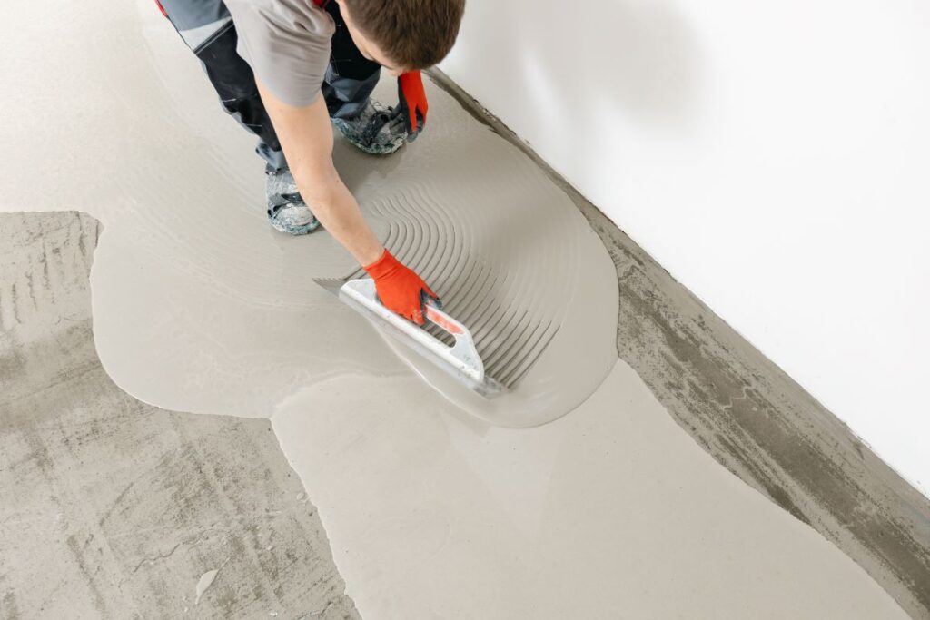 Worker spreading mortar on floor with trowel.