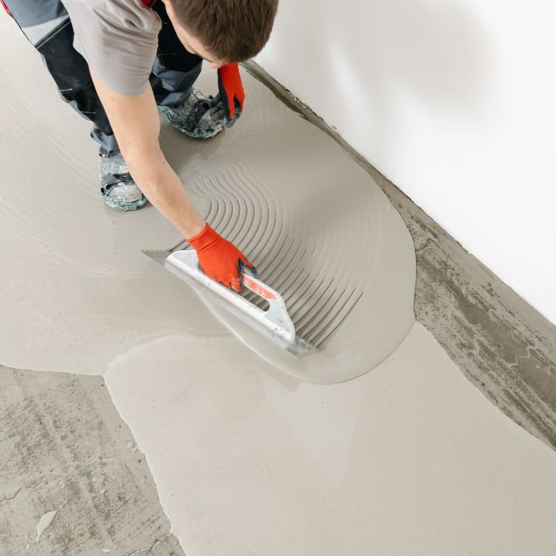 Worker spreading mortar on floor with trowel.