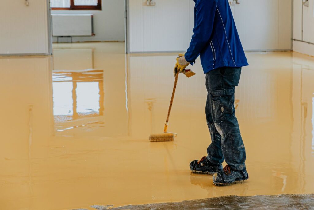 Worker applying epoxy floor coating in room