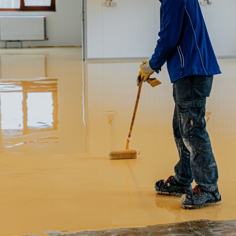 Worker applying epoxy floor coating in room