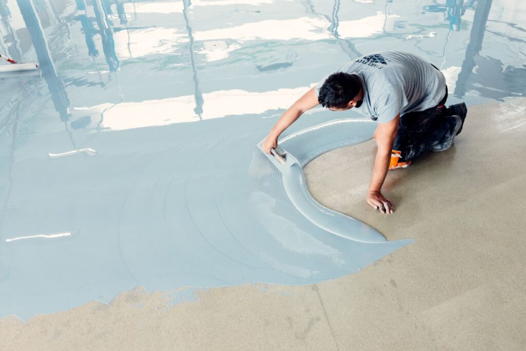 Worker applying epoxy floor coating with tool.