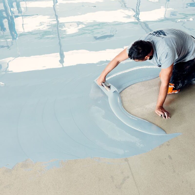 Worker applying epoxy floor coating with tool.