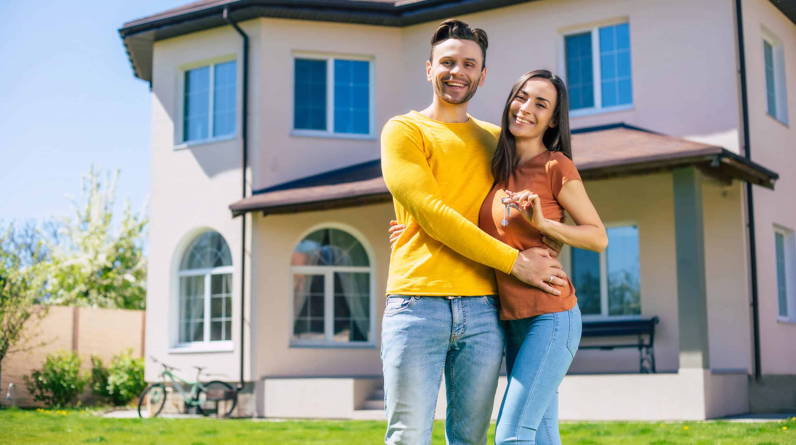 Happy couple with house keys in front of home