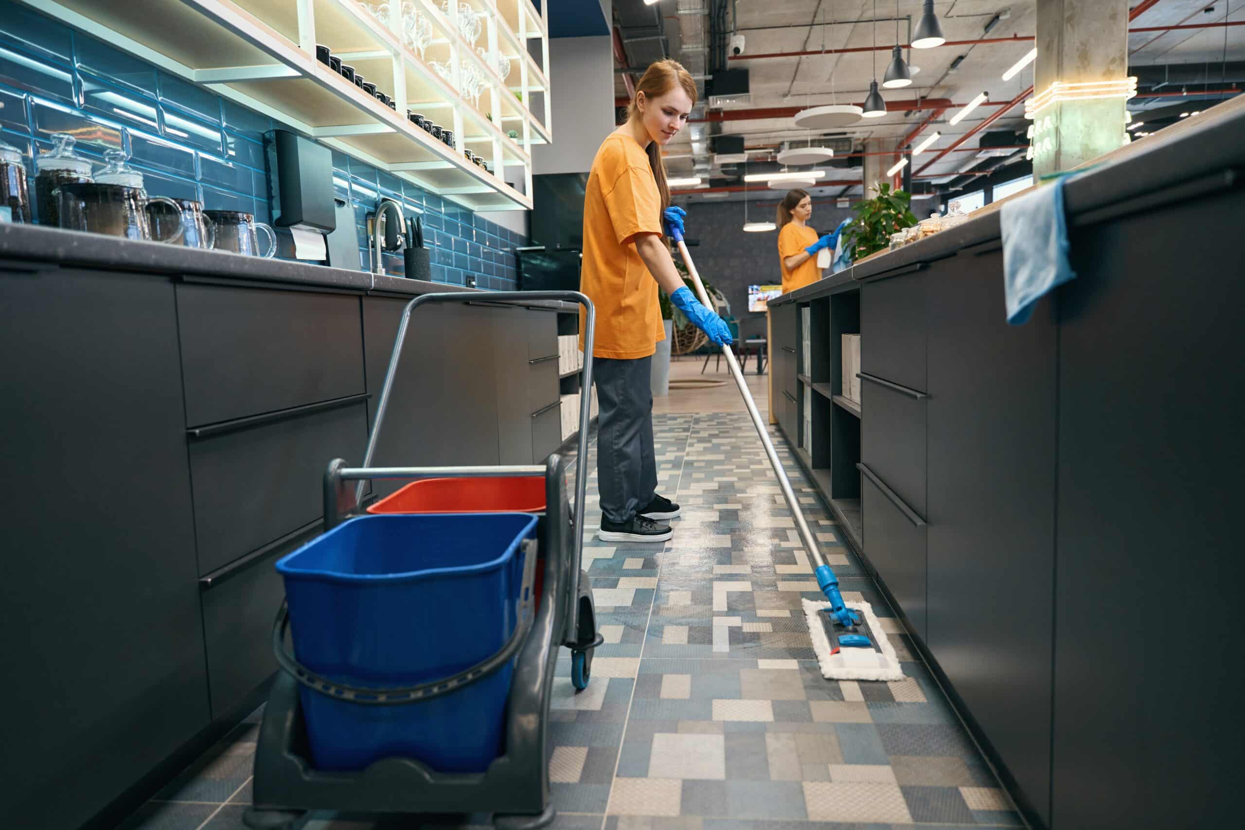 Person mopping office floor with cleaning cart nearby.