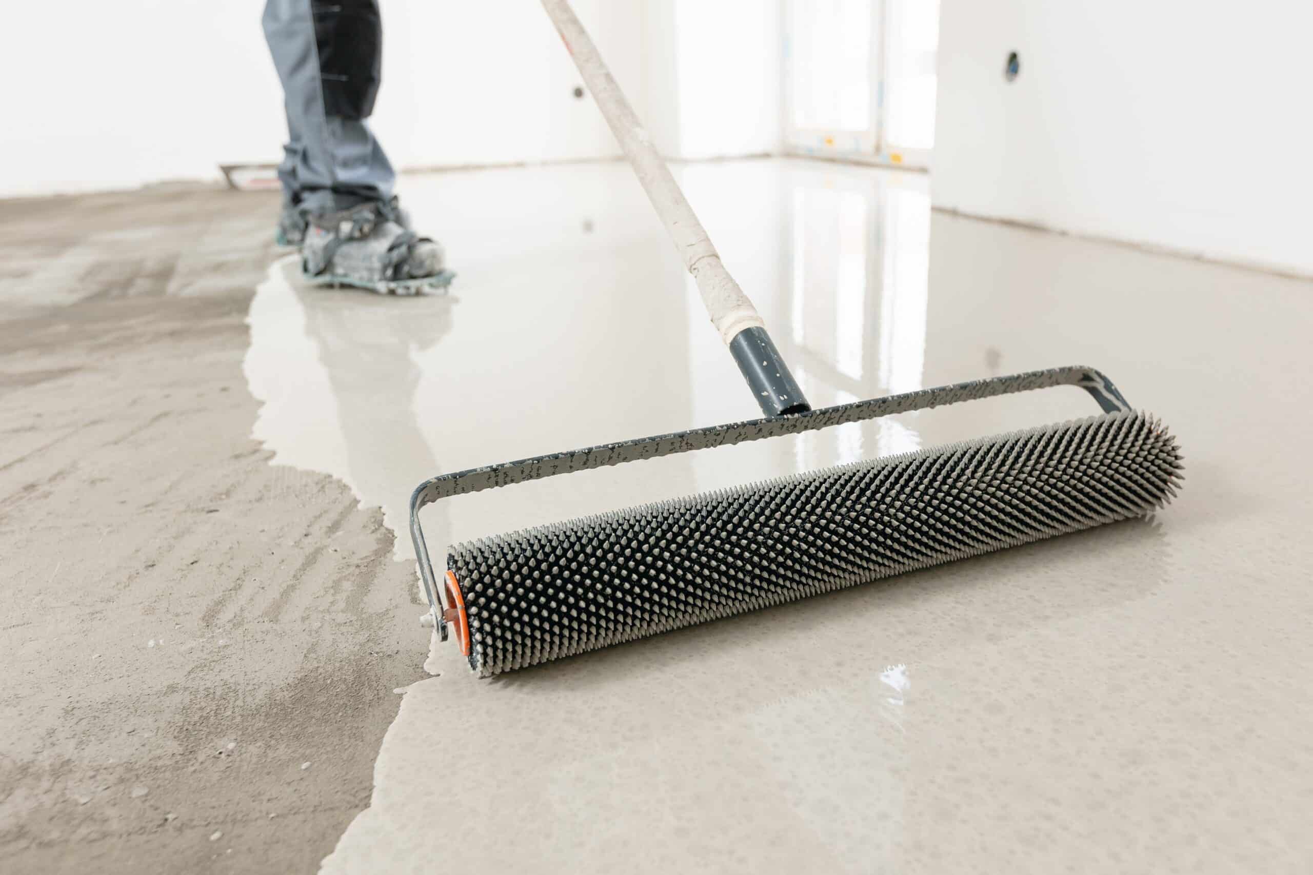 Worker applying self-leveling floor with spike roller