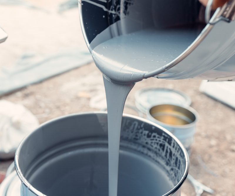 Gray paint pouring into bucket outdoors
