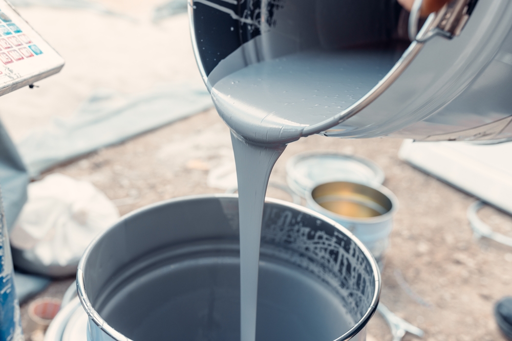 Gray paint pouring into bucket outdoors